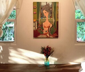 A framed artwork on a wall, a vase with flowers on a table, and a window with a view of greenery. - Oceanfront Artistic Escape in Cabuya (Cabuya)