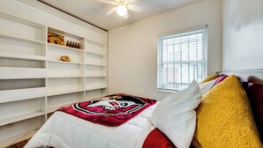 Ein Schlafzimmer mit einem Bett, einem Deckenventilator, einem Fenster und einer eingebauten Bücherreol.
