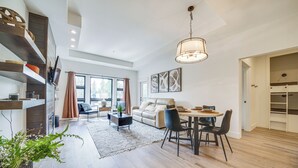 A modern living room with a sofa, dining table, and chairs, a staircase with shelves, and a large window. - Suncadia Resort Condo Near Trails & River Access! (Cle Elum)