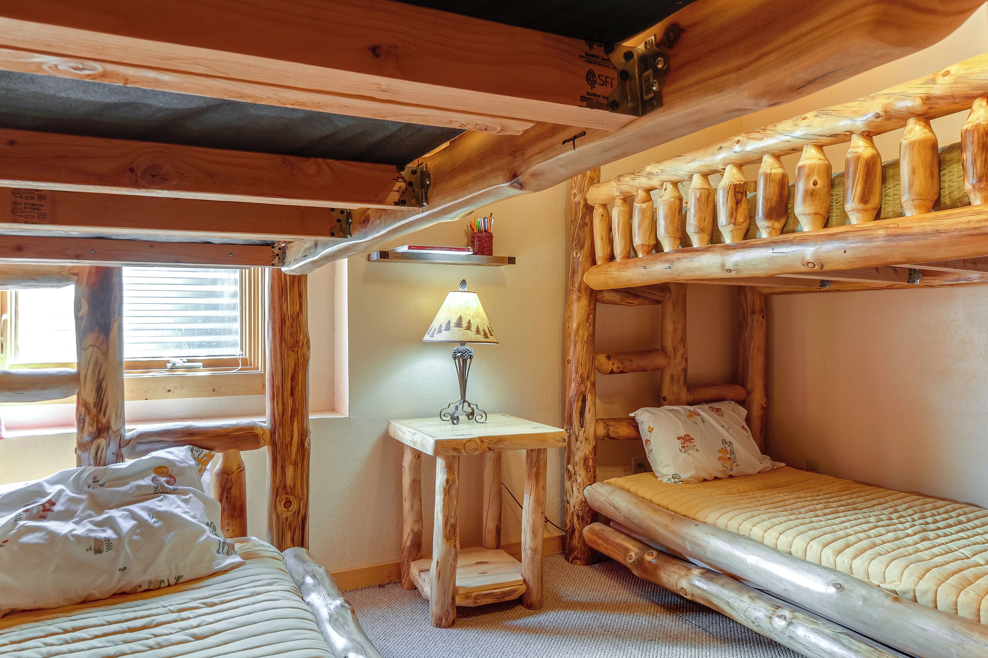 Una habitación rústica de madera con una litera, una mesita con una lámpara y una ventana con persianas.