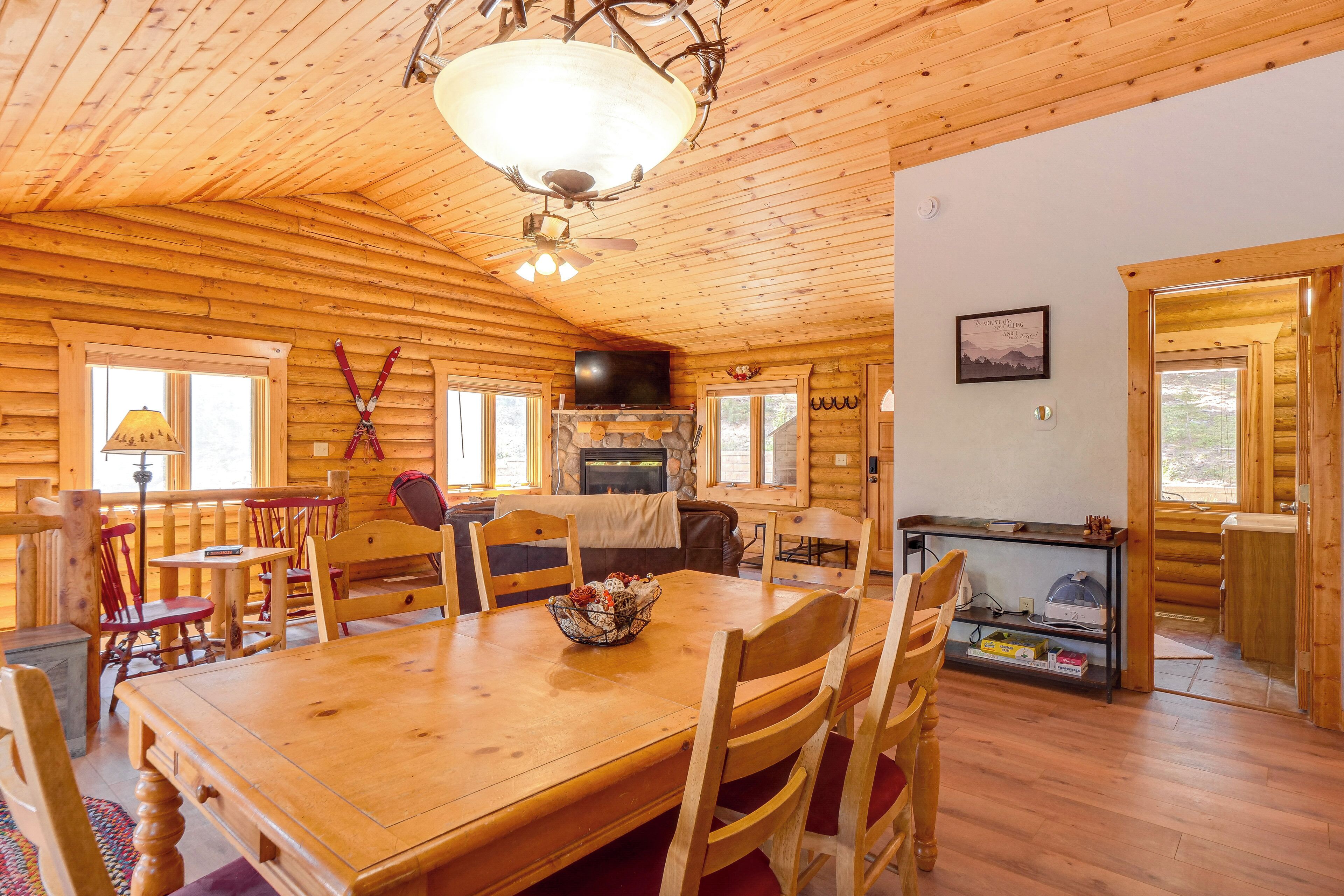 A wooden cabin interior with a dining table, chairs, a fireplace, a television, and a stone wall.