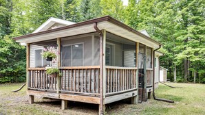 A wooden cabin with a covered porch, a screened window, and a hanging flower pot. - Private UP Escape Near Lake Superior (Pelkie)