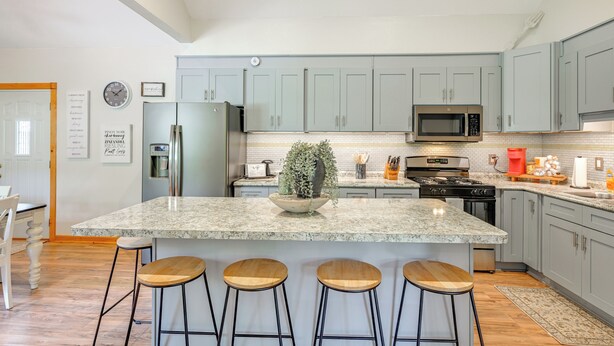 A modern kitchen with granite countertops, bar stools, a central island, and light grey cabinetry.