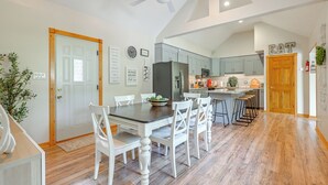 A modern kitchen with white cabinets, a central island, and a dining area with white chairs.