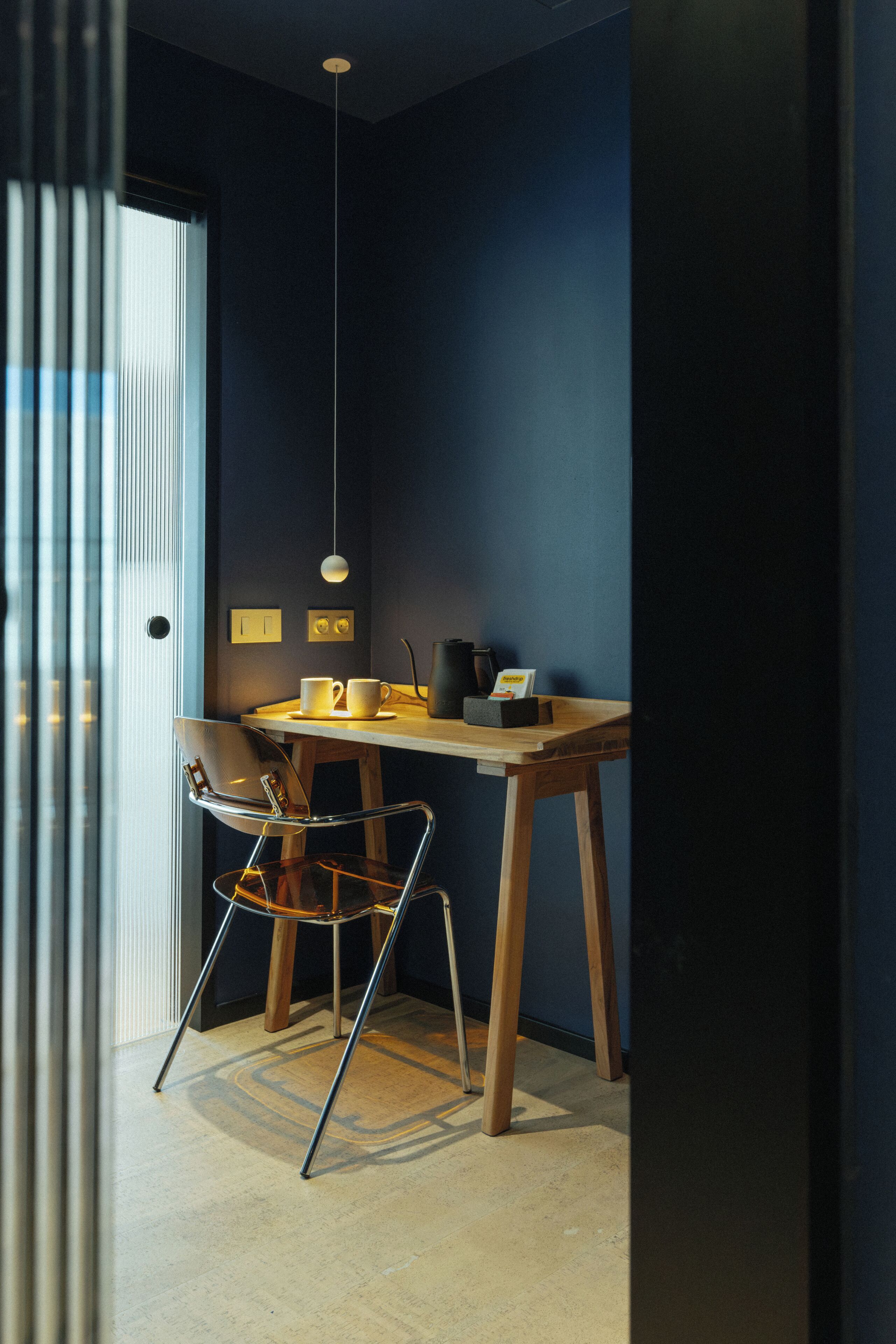 A room with a wooden table, a chair, a hanging light fixture, and a door.