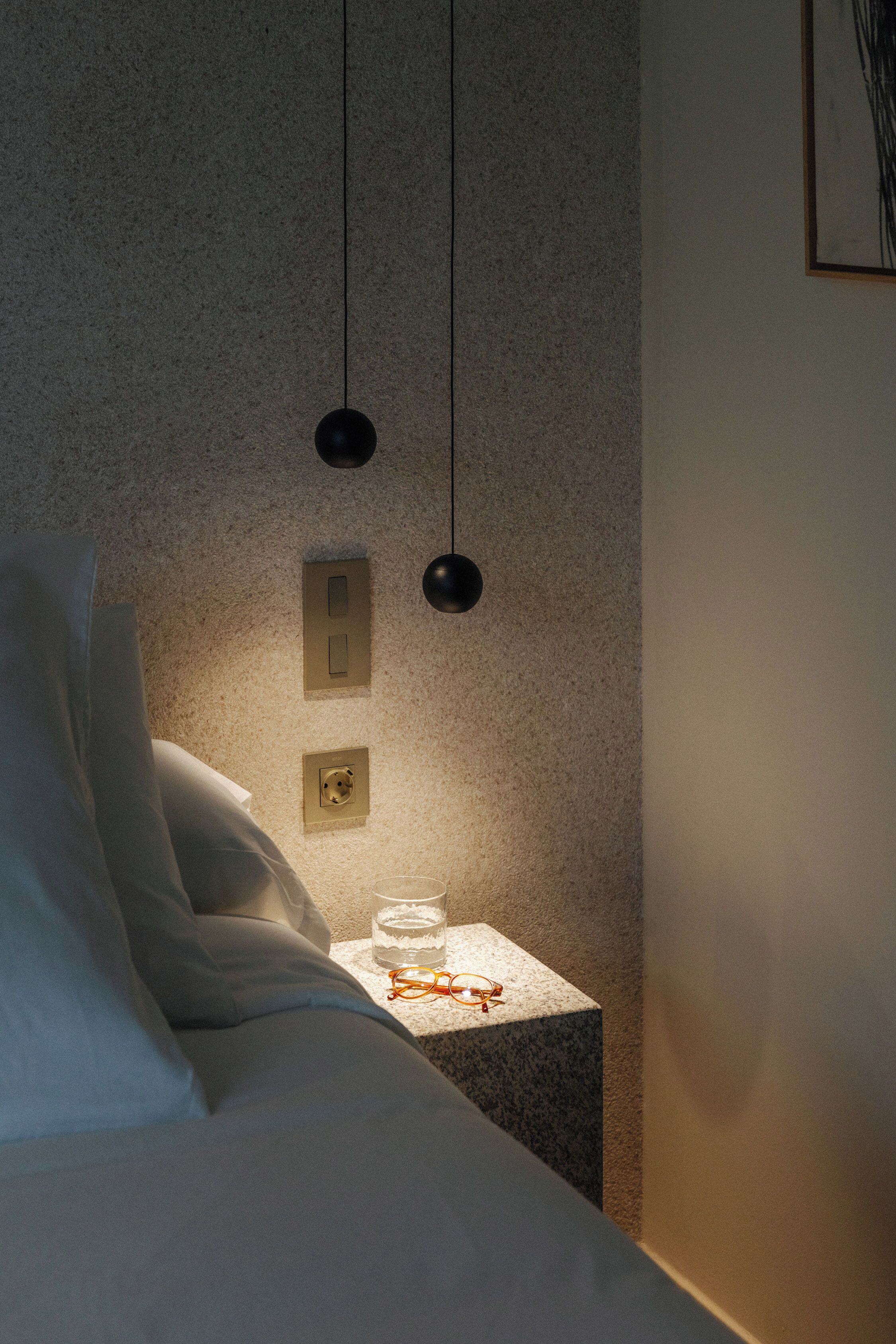 A bedroom with a bed, bedside table, and a wall-mounted light fixture.