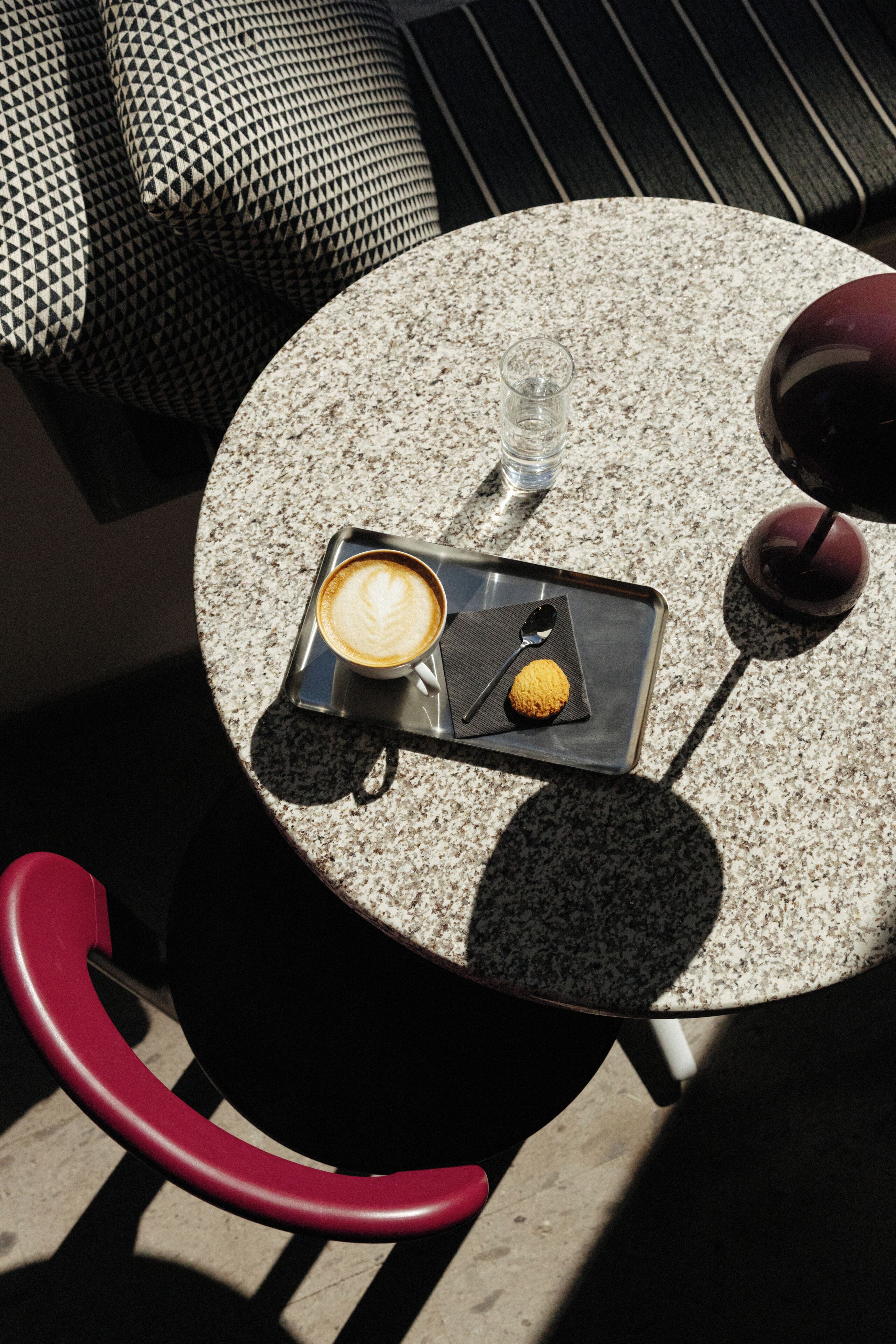 A round table with a cup of coffee, a spoon, and a small pastry.