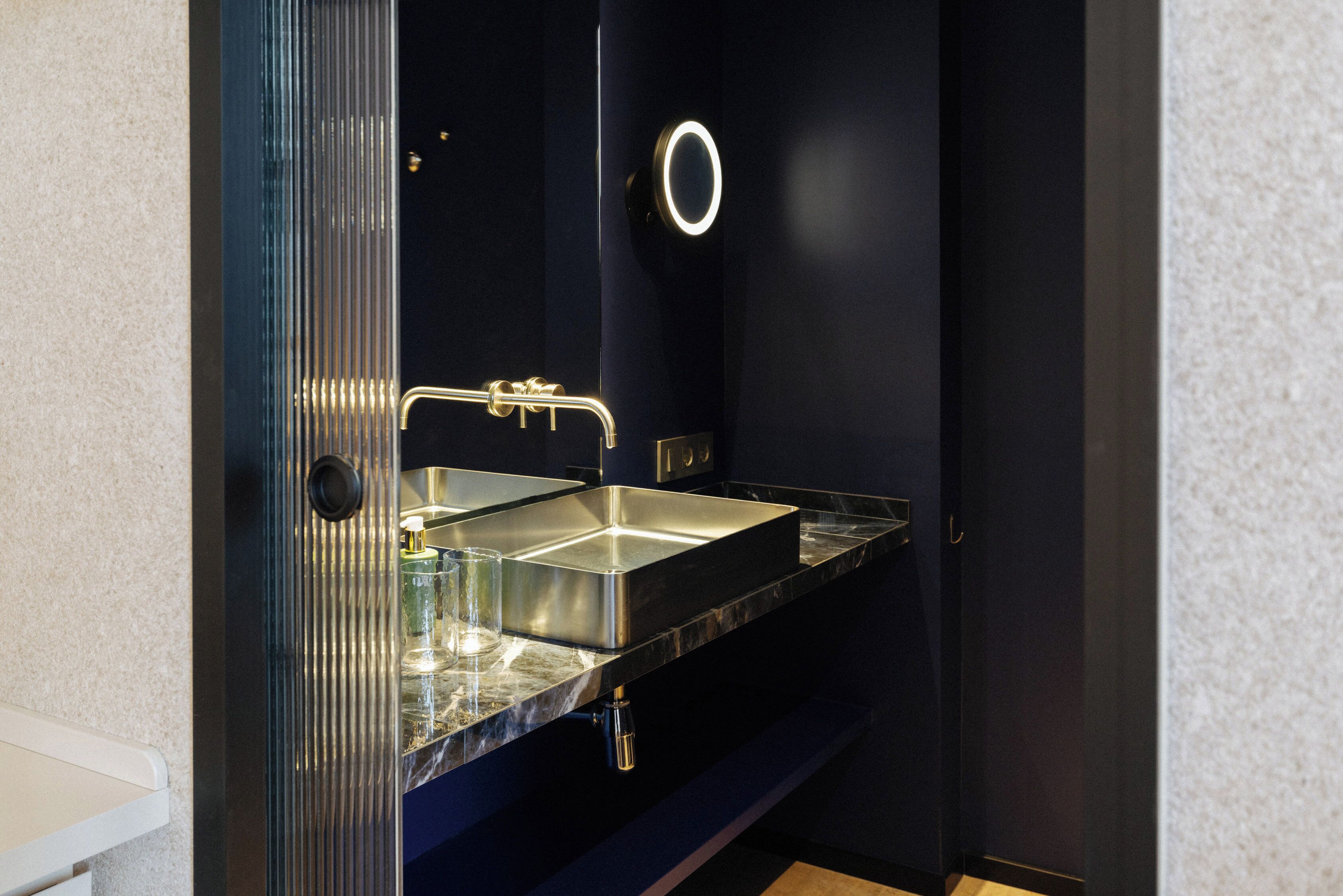 A modern bathroom with a dark blue wall, a stainless steel sink, and a glass partition.