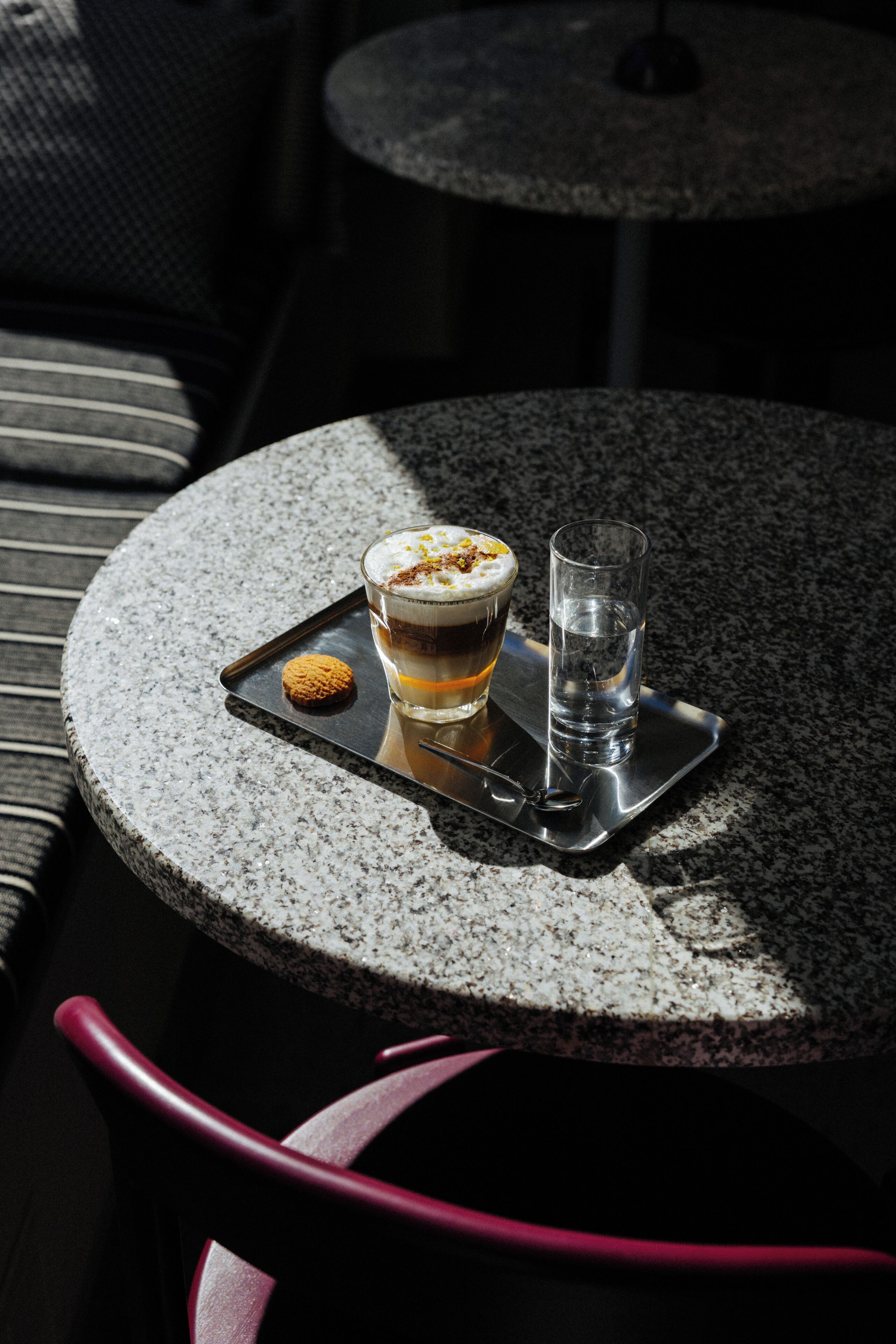 A round table with a tray holding a glass of water, a glass of coffee, and a cookie.