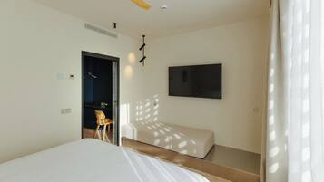 A modern hotel room with a bed, a TV mounted on the wall, a ceiling fan, and a door leading to a bathroom.