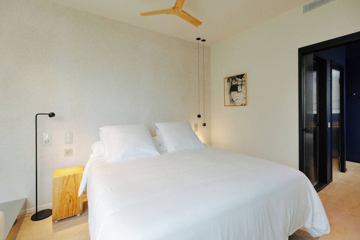 Quarto com cama, mesa de cabeceira, abajur e ventilador de teto.