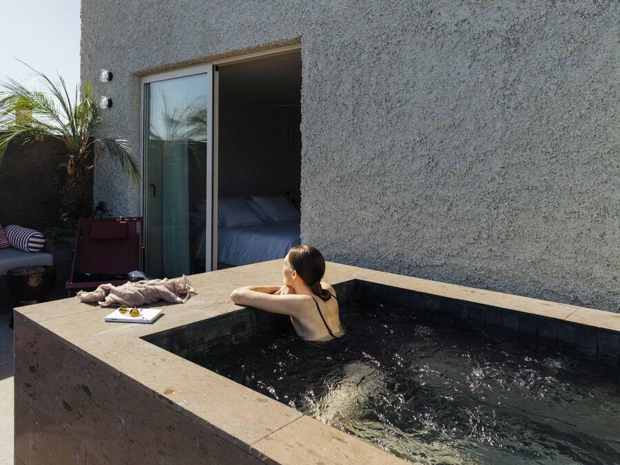 Una mujer descansando en un jacuzzi con un libro y gafas de sol al lado.