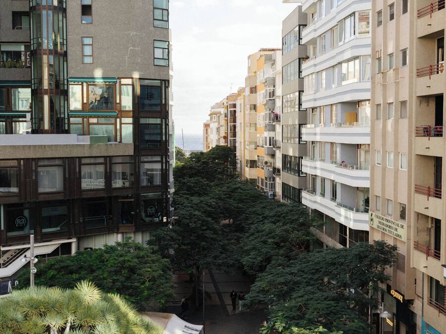 A multi-story building with balconies, a covered walkway, and a tree in the foreground.