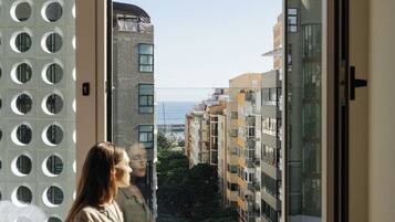 Alguém sentado perto de uma janela, com vista para edifícios e um corpo de água.