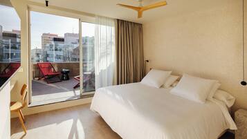 Una habitación de hotel con una cama grande, un balcón con sillas rojas y vistas a la ciudad.