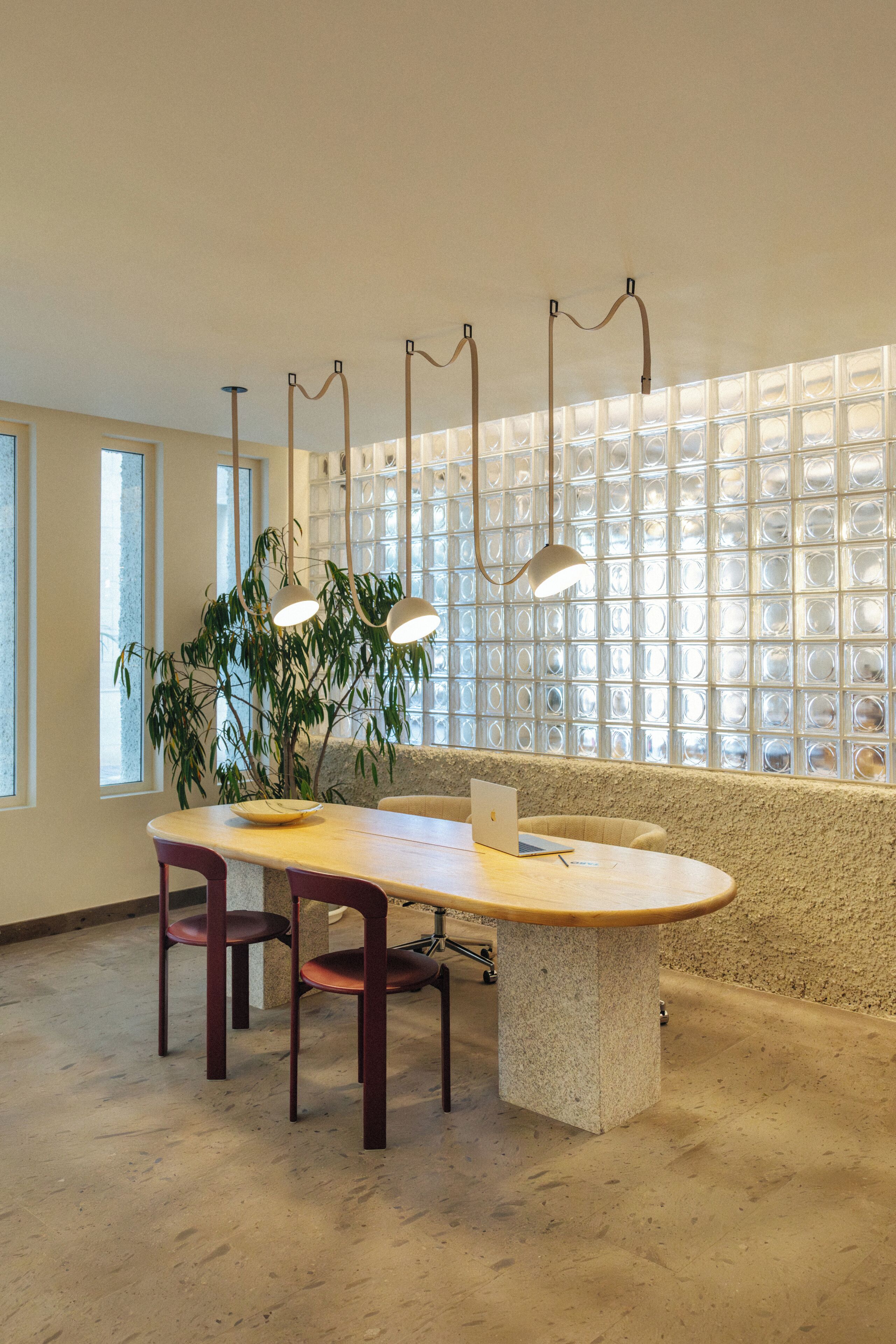 A modern dining area with a round table, two chairs, a laptop, and a potted plant.