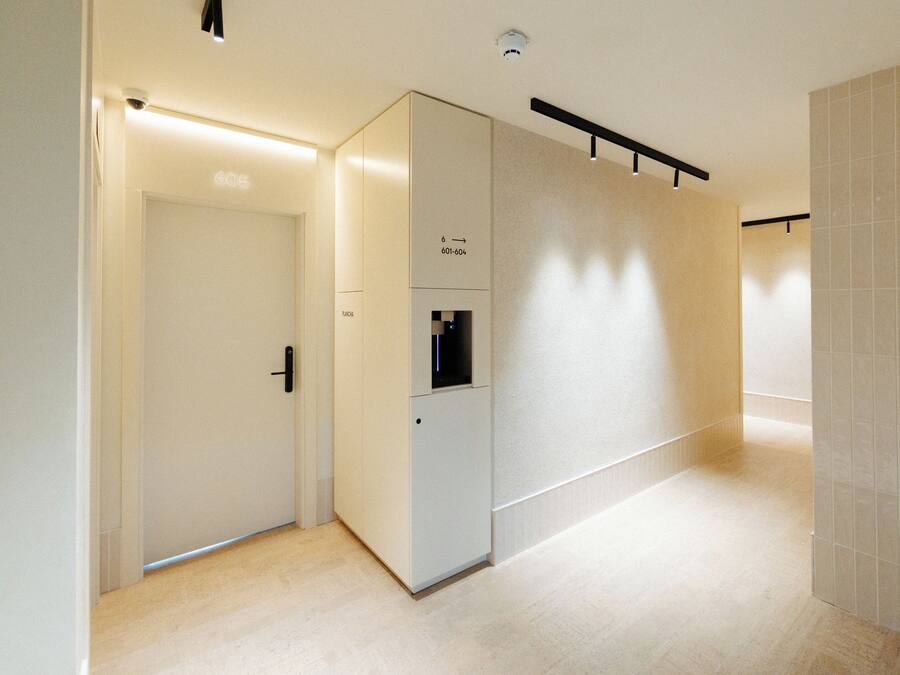 A hallway with a door, a vending machine, and a wall-mounted light fixture.
