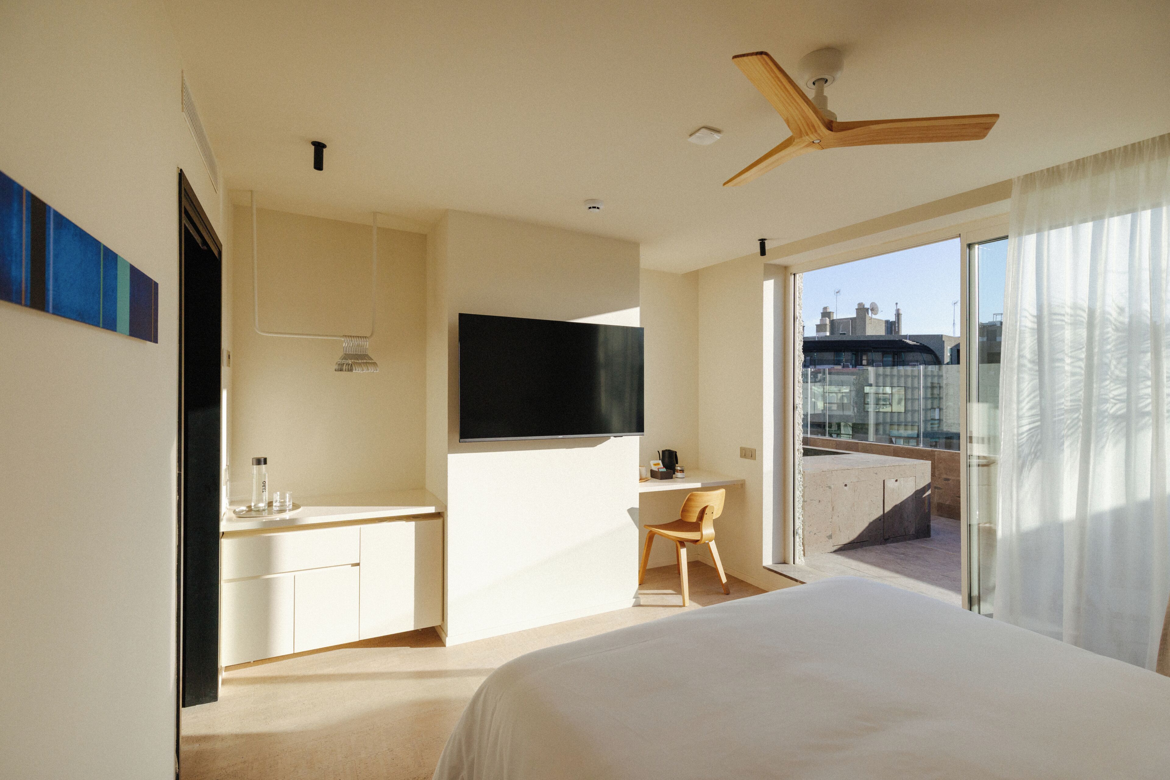 A hotel room with a bed, a desk, a chair, a TV, and a balcony with a view.