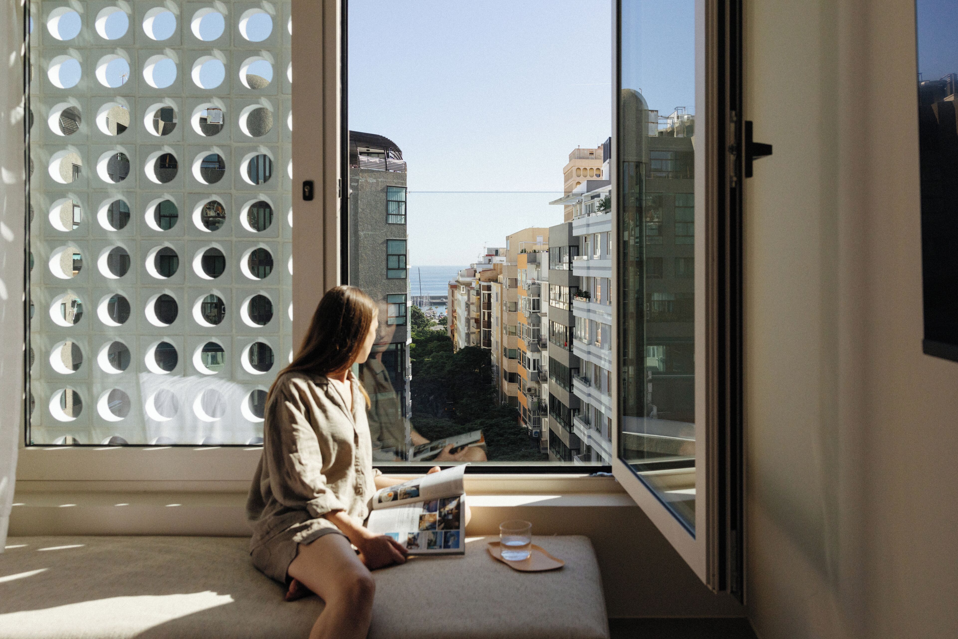 A person sitting by a large window with a view of a cityscape and buildings.