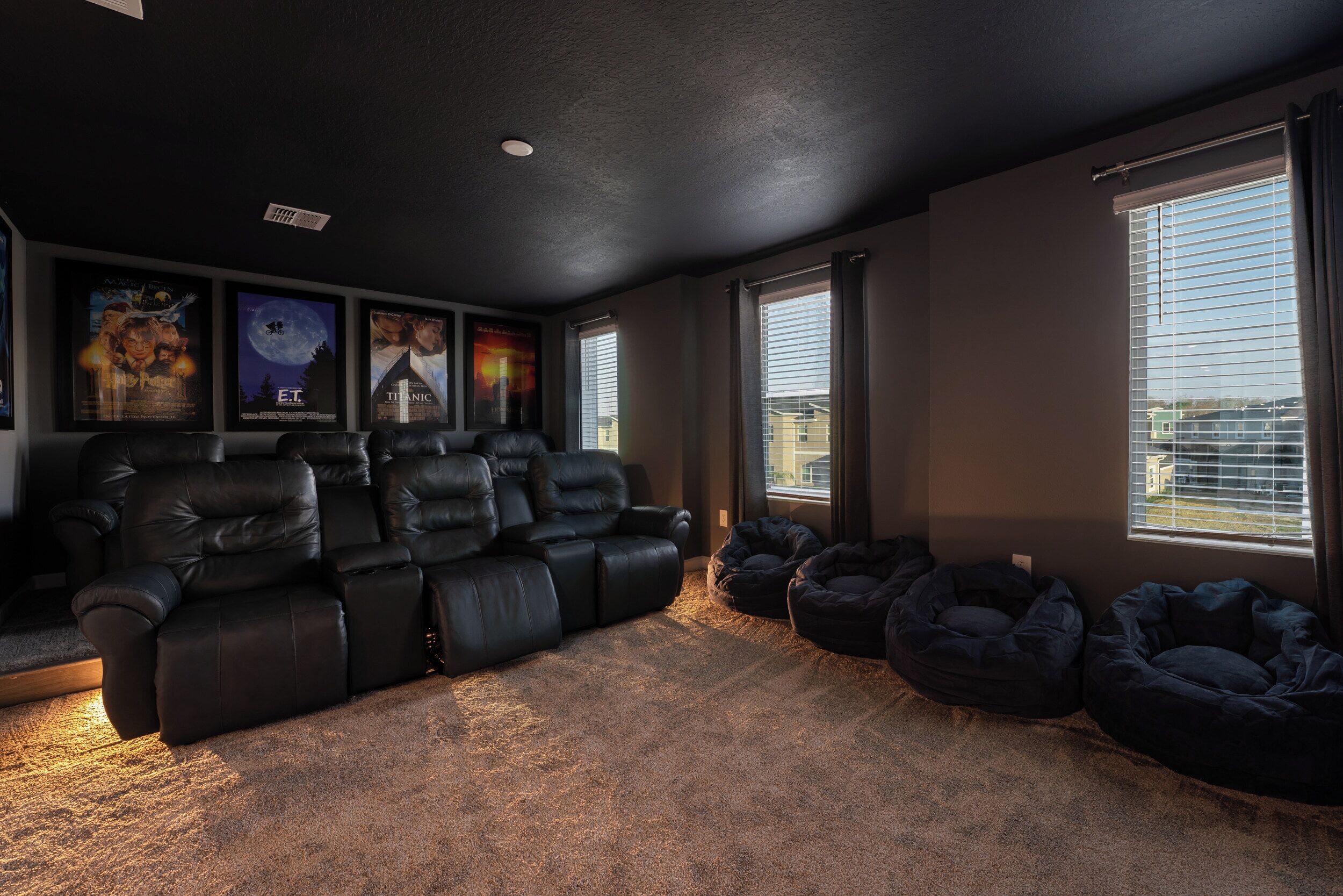 A home theater room with a black leather recliner sofa, bean bag chairs, and movie posters on the wall.