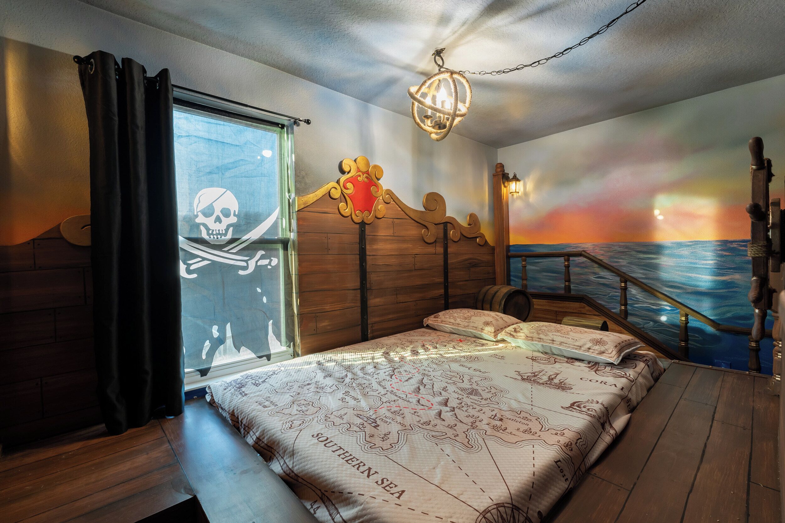 A bedroom with a bed, a window with curtains, a wooden headboard, a wall mural, and a staircase.