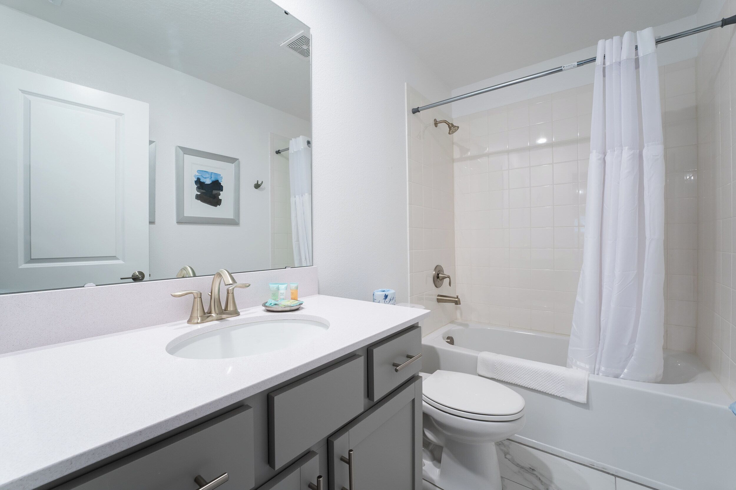 A bathroom with a white sink, two faucets, a mirror, a toilet, and a bathtub with a shower curtain.