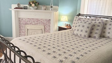 A bedroom with a bed, a fireplace, a wall-mounted picture, and a window with a wreath.