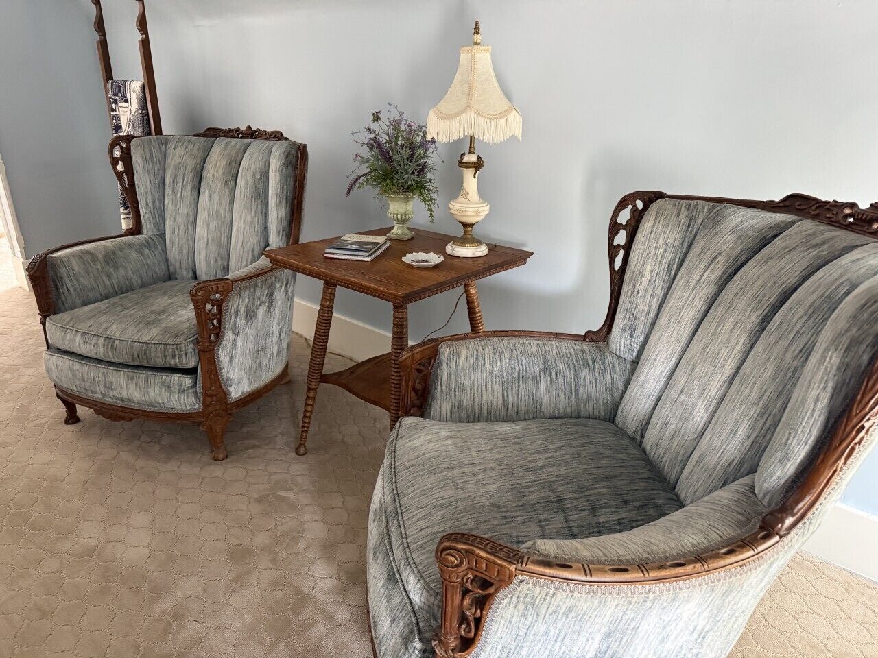 Two upholstered armchairs with wooden frames and a small wooden table with a lamp and a vase of flowers.