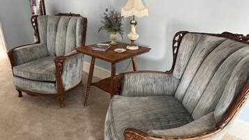 Two upholstered armchairs with wooden frames and a small wooden table with a lamp and a vase of flowers.