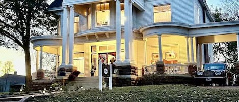 A large, two-story house with a wrap-around porch, multiple windows, and a well-maintained lawn.