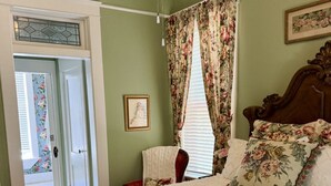 A bedroom with a bed, a wooden headboard, a door, and a window with floral curtains. - The Lynnie Ann at The Judge`s Chamber (Guthrie)