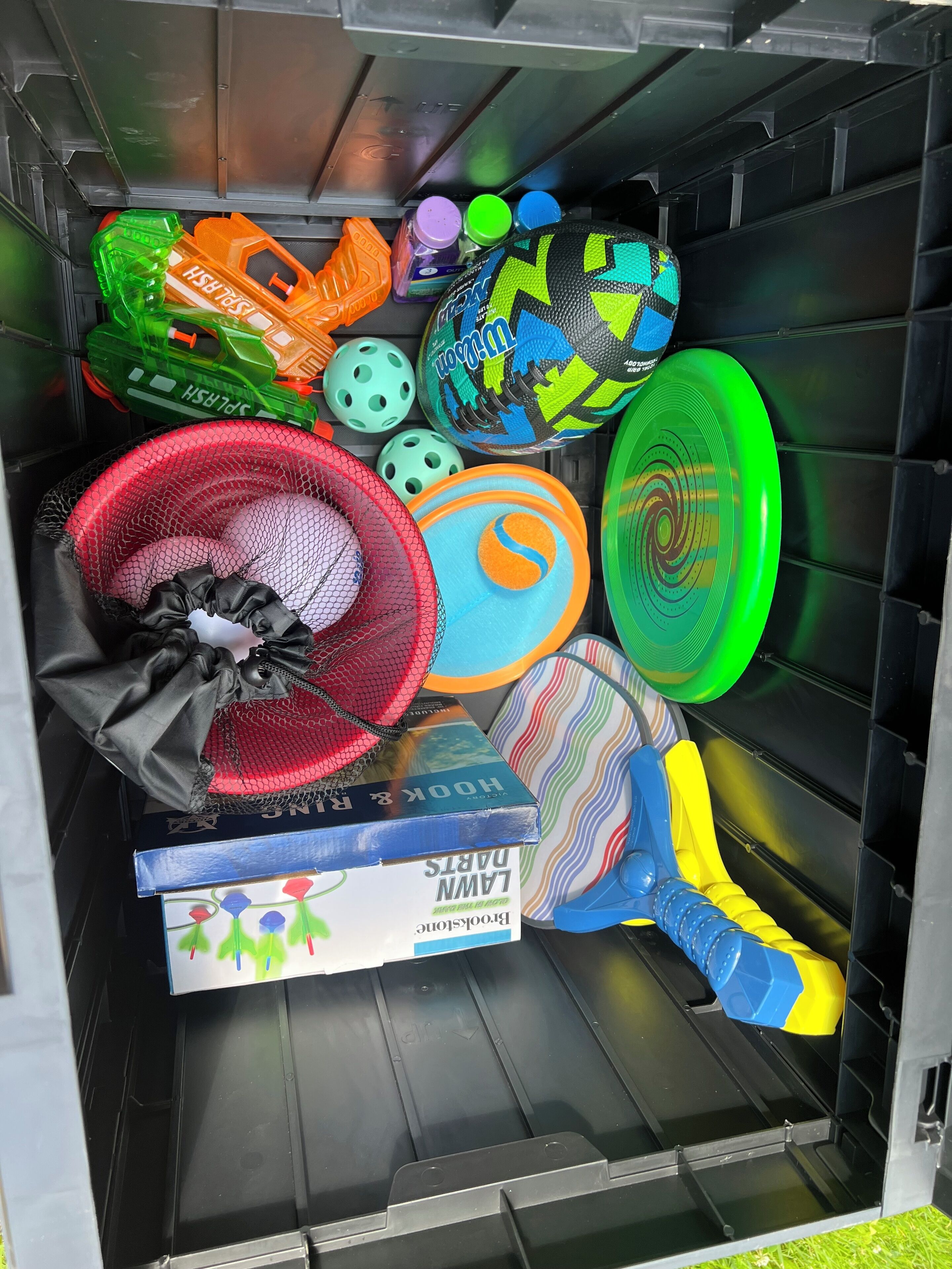 A storage unit with various sports equipment, including a netted bag, multiple frisbees, and a colorful toy.