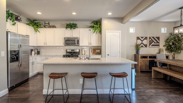 Una cocina moderna con armarios blancos, electrodomésticos de acero inoxidable, una isla grande con taburetes y plantas decorativas.