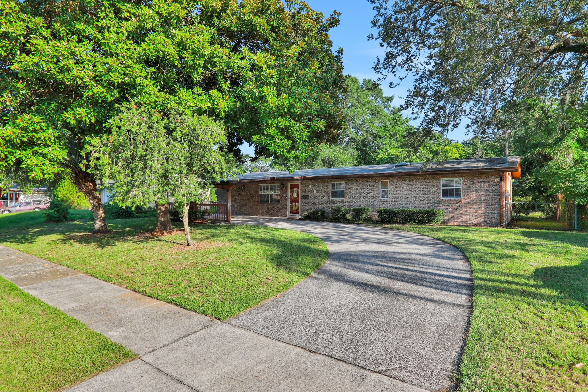 A single-story brick house with a front yard, a driveway, and a large tree.