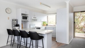 Une cuisine moderne avec des meubles blancs, un îlot central doté de tabourets, un four à micro-ondes et une horloge murale.