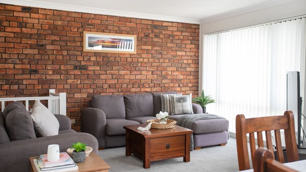 A living room with a brick wall, a grey sofa set, a wooden coffee table, and a white-framed picture.