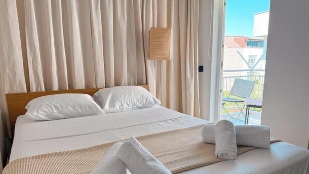 Ein Hotelzimmer mit Bett, weißen Laken, einem Holz-Kopfteil und Blick ins Freie.