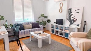 Ein modernes Wohnzimmer mit Sofa, Couchtisch und TV-Möbel. Zimmerpflanzen, ein Gemälde und eine Gitarre sind ebenfalls vorhanden.