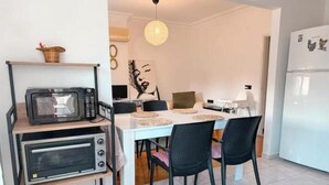 Eine kleine Küche mit Mikrowelle, Toaster und Kühlschrank. Ein Esstisch mit Stühlen und eine Hängelampe sind vorhanden.