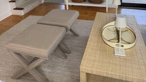 A modern living room with a staircase, a white console table with baskets, a large mirror, and a view of the outdoors.