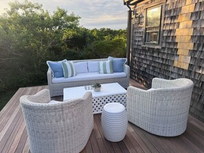 Un espacio exterior con mobiliario de mimbre, una mesa blanca y un sofá con cojines a rayas.