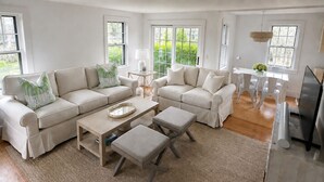 A modern living room with a sectional sofa, a coffee table, ottomans, and a dining area with a table and chairs.