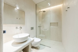 Uma casa de banho moderna com uma grande lavatório branca, uma sanita e zona de duche separada por vidro.