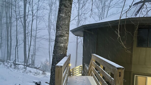 Een houten hut met een sneeuwbedekte veranda en uitzicht op een bebost gebied.