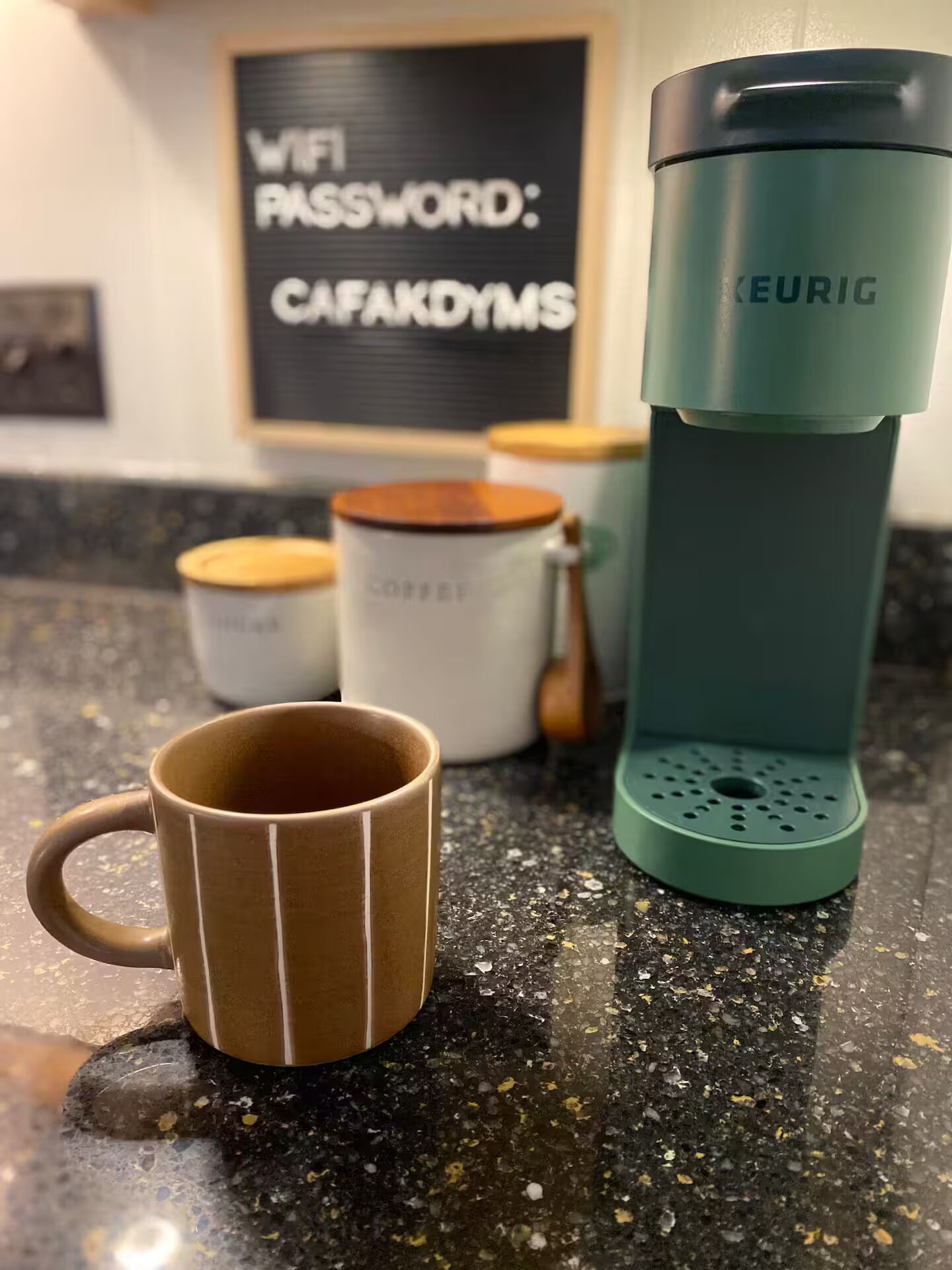 A kitchen counter with a coffee maker, a mug, and a container labeled "COFFEE".