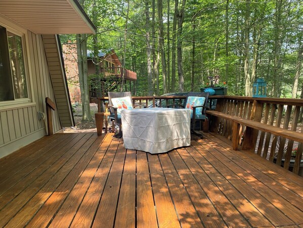 Una terraza de madera con una mesa y sillas, rodeada por barandilla de madera y árboles.