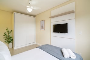 A hotel room with a bed, a TV mounted on the wall, a wardrobe, and a potted plant. - Apart With Barbecue 600m From the Beach Rpn0101 (Florianópolis)