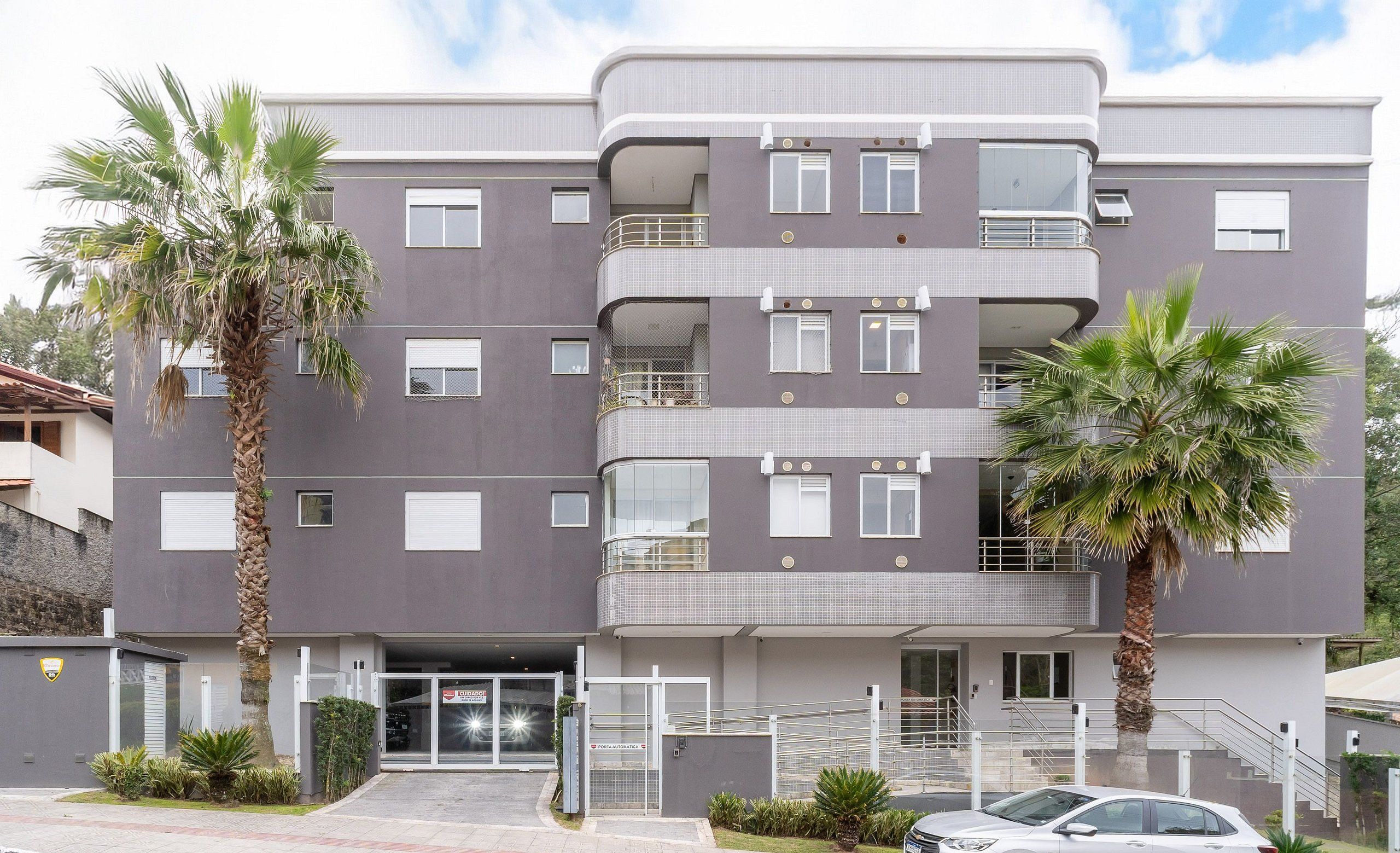 A multi-story residential building with balconies, a gated entrance, and a parked car.