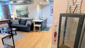 A modern living room with a wooden ceiling, a sofa, a coffee table, and a kitchen area with a sink and countertop.