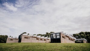 Un bâtiment moderne à la façade en briques et aux grandes fenêtres, entouré d’une pelouse et d’arbres.